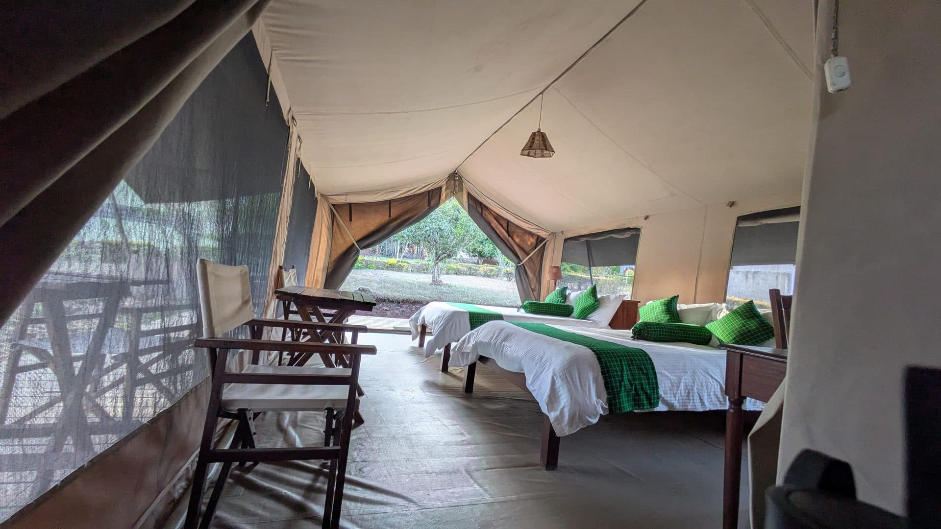 Pitched tent with twin beds made up and chairs facing the open canvas front